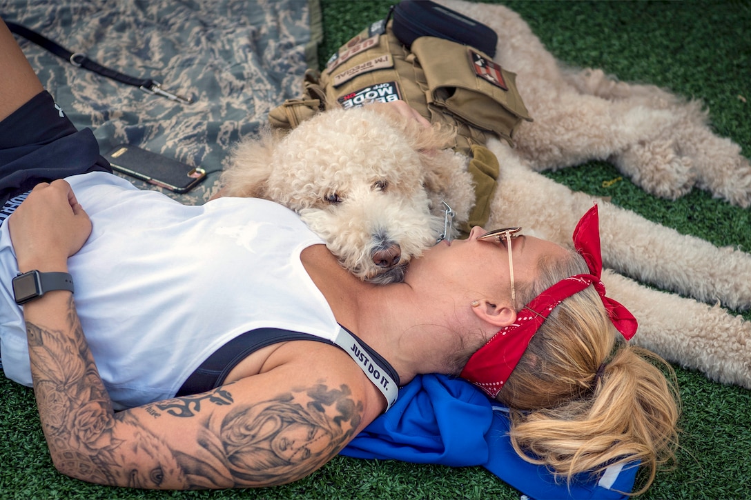 A woman in athletic wear lies down with a doodle-type dog with a service dog vest.