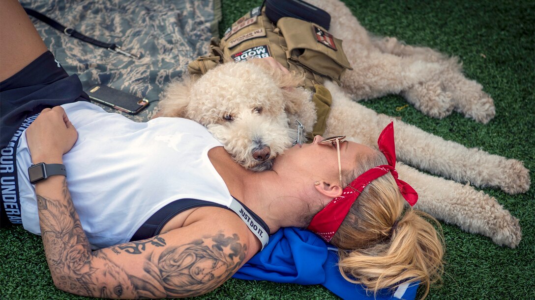 A woman in athletic wear lies down with a doodle-type dog with a service dog vest.