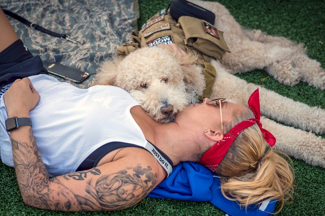 A woman in athletic wear lies down with a doodle-type dog with a service dog vest.