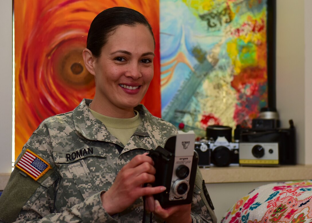 U.S. Army Spc. Wilmarys Roman Rivera, Headquarters and Headquarters Company, 10th Battalion, 7th Transportation Brigade (Expeditionary) tactical power generation specialist, holds a camera at Joint Base Langley-Eustis, Virginia, April 20, 2018. Roman Rivera was an established commercial photographer and photography instructor prior to enlisting in the Army. (U.S. Air Force photo by Airman 1st Class Monica Roybal)