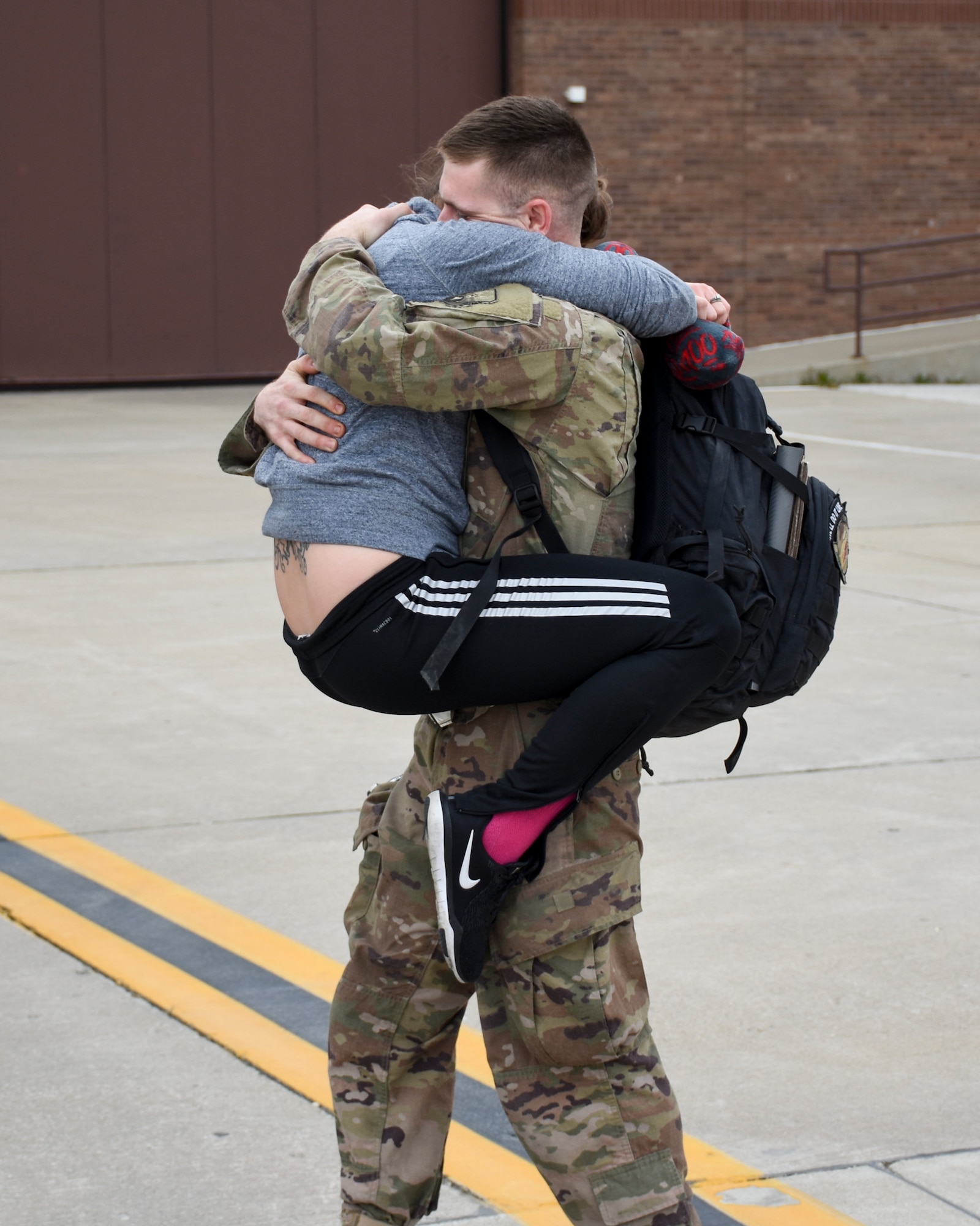 A woman leaps into the arms of her returning Airman as he approaches the waiting families outside the 5-bay.
