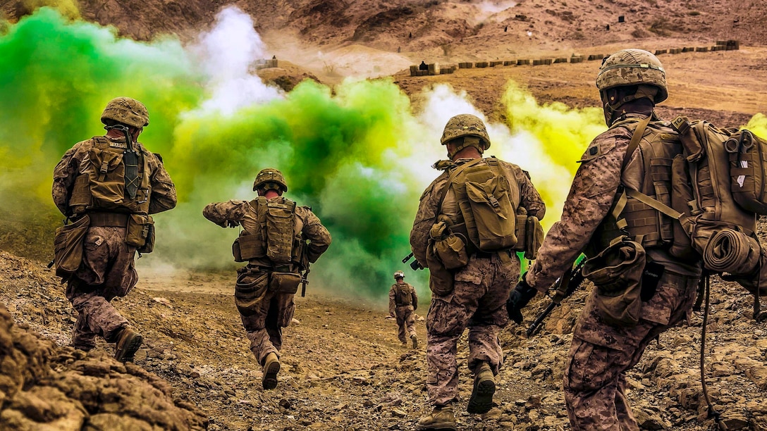 Marines run down a hill toward green smoke.