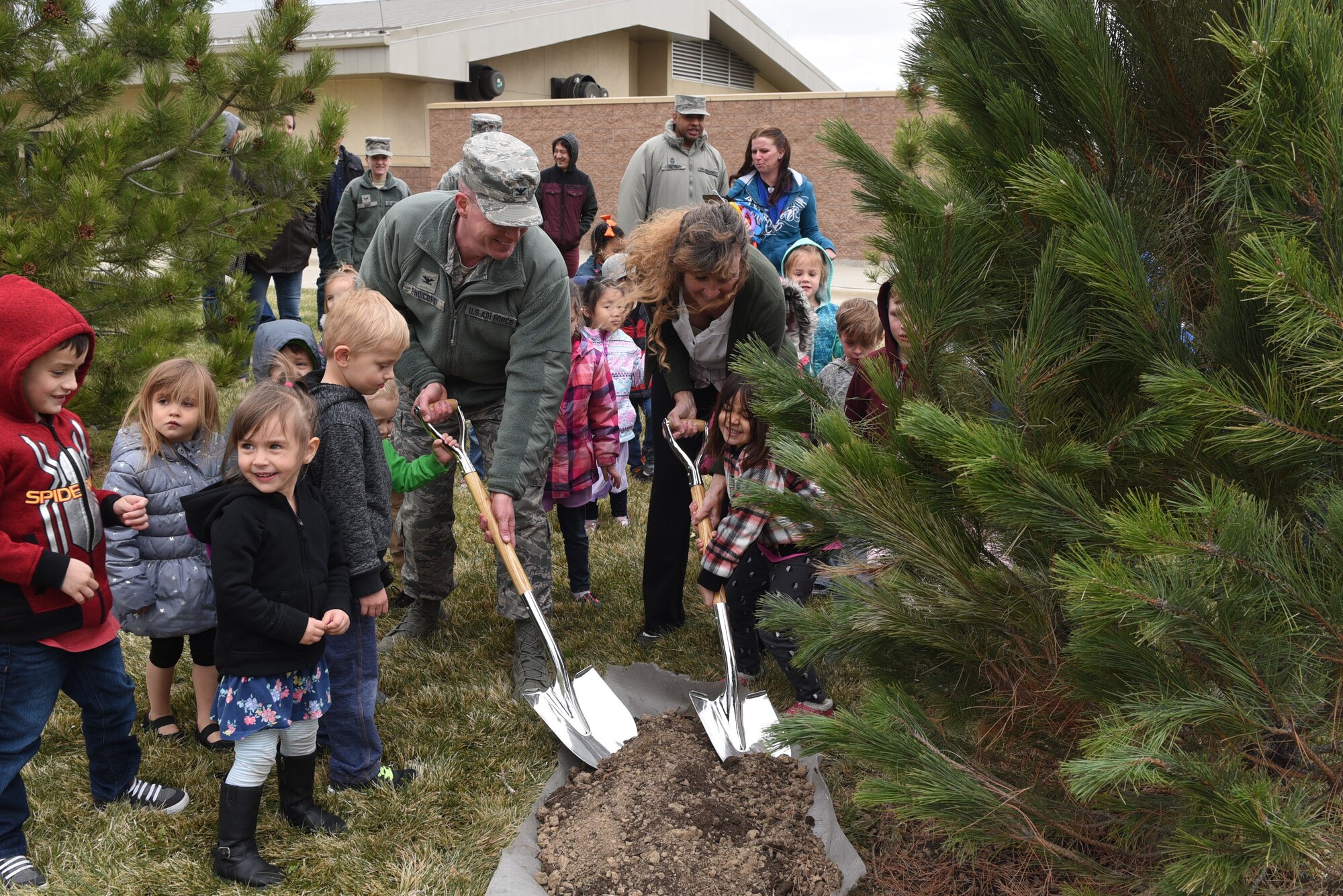 Col. Troy L. Endicott, 460th Space Wing commander, and Ms. Nancy Klasky, a member of the Community Forestry Division for Colorado State, ceremoniously pour dirt on a pine tree planted in honor of Arbor Day, April 26, 2018, on Buckley Air Force Base, Colorado. Children from the Child Development Center participated in the event by helping pour dirt around the base of the tree as well. (U.S. Air Force Photo by Senior Airman Jessica B. Kind)