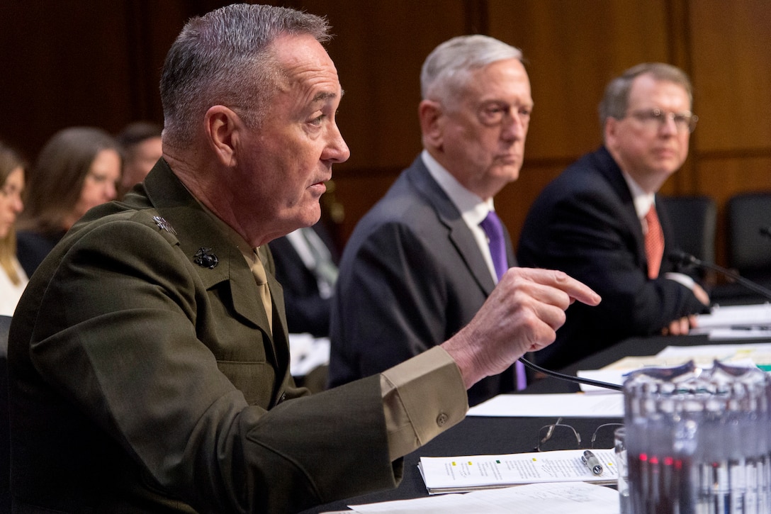 Defense Department leaders sit behind a desk.