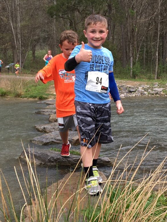 This young boy gives a thumbs up as he crosses Hatchery Creek in Jamestown, Ky., during the third annual Trout Trot 5K April 14, 2018 at the Wolf Creek National Fish Hatchery and Kendal Recreation Area below Wolf Creek Dam. The event also kicked off the recreation season at Lake Cumberland, which is operated by the U.S. Army Corps of Engineers Nashville District. (USACE photo by Park Ranger Cody Pyles)