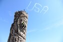A young man climbs a rock wall while a plane draws “USA” in the sky during 2018 Wings Over Columbus April 21, 2018 at Columbus Air Force Base, Mississippi. Along with the aerial performances, rock-climbing and other carnival-type attractions were present at the air show. (U.S. Air Force photo by Airman 1st Class Beaux Hebert)