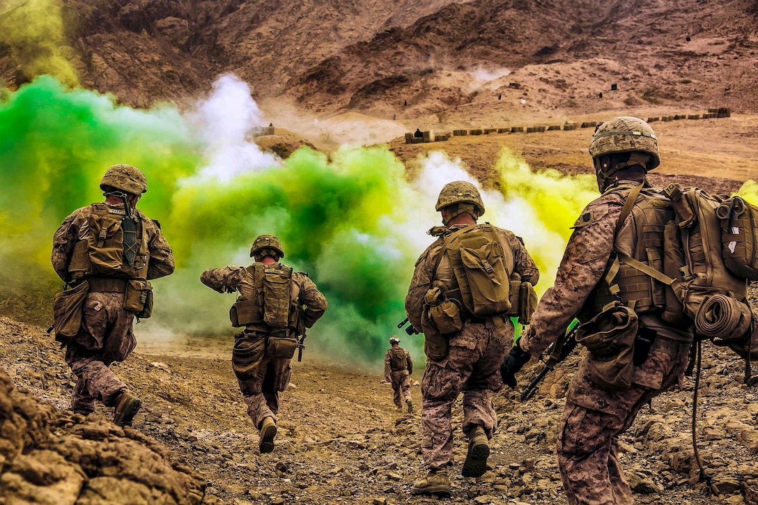 Marines run down a hill toward green smoke.