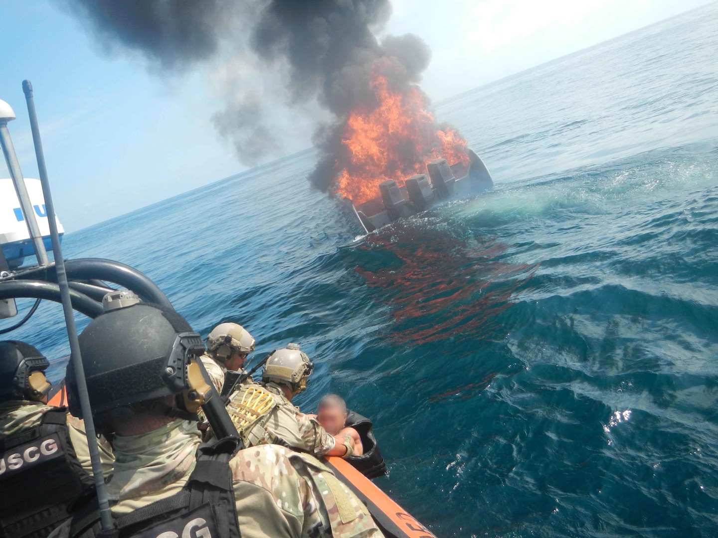 suspected smuggler who jumped from his burning vessel, in background, is pulled aboard an interceptor boat.