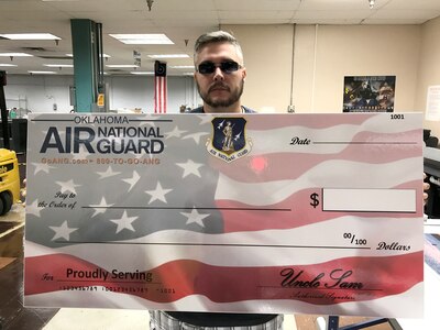 Kevin Hogan, DMS employee at the Tinker AFB facility, holds up the check created for the Oklahoma Air National Guard’s recruitment campaign.