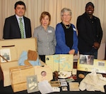 IMAGE: VIRGINIA BEACH, Va. (April 25, 2018) - Vivian Margulies and Lynn Woods of the United Jewish Federation of Tidewater pause at a table filled with mementoes and reproductions from the life of Dana Cohen during a commemoration held at Naval Surface Warfare Center Dahlgren Division Dam Neck Activity. Margulies and Woods spoke about the life of Cohen - a Hampton Roads resident - in their presentation entitled, 'What We Carry', to military and civilian personnel commemorating Holocaust Remembrance Day. NSWCDD Dam Neck Activity engineer Roberto Garcia and Equal Employment Opportunity specialist Marcus Matthews coordinated the visit. Standing left to right are Garcia, Margulies, Woods and Matthews. For more on Cohen's story, visit http://jewishva.org/node/746.