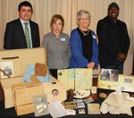 IMAGE: VIRGINIA BEACH, Va. (April 25, 2018) - Vivian Margulies and Lynn Woods of the United Jewish Federation of Tidewater pause at a table filled with mementoes and reproductions from the life of Dana Cohen during a commemoration held at Naval Surface Warfare Center Dahlgren Division Dam Neck Activity. Margulies and Woods spoke about the life of Cohen - a Hampton Roads resident - in their presentation entitled, 'What We Carry', to military and civilian personnel commemorating Holocaust Remembrance Day. NSWCDD Dam Neck Activity engineer Roberto Garcia and Equal Employment Opportunity specialist Marcus Matthews coordinated the visit. Standing left to right are Garcia, Margulies, Woods and Matthews. For more on Cohen's story, visit http://jewishva.org/node/746.