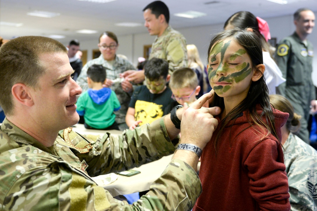 An airman puts green face paint on a child.