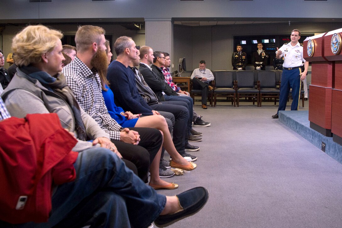 A group of people sit and look at a soldier speaking.