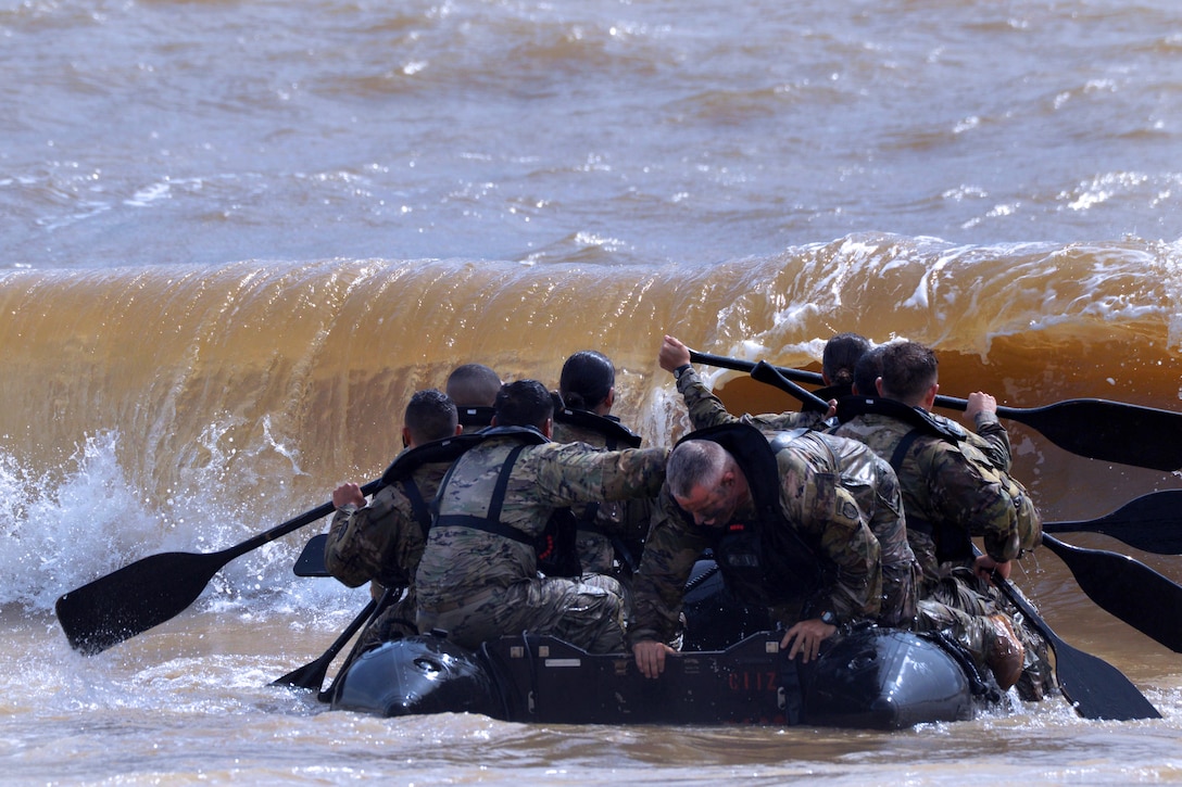 Soldiers get hit by a wave as they paddle their watercraft.