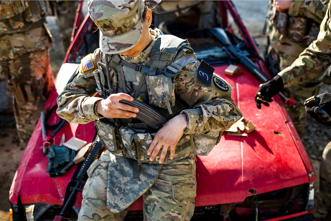 A soldier loads a magazine into her vest.