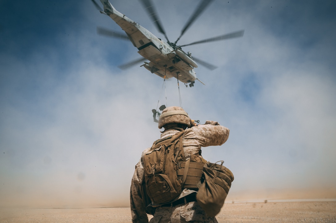 A Marine with combat logistics battalion 8, 2 marine logistics group watches a CH-53E Super Stallion carry away M777 Howitzer at Sand hill Marine Corps Air Ground Combat Center, Twentynine Palms, Calif., Apr 27, 2018, as a part of Integrated Training Exercise 3-18. The purpose of ITX is to create a challenging, realistic training environment that produces combat-ready forces capable of operating as an integrated MAGTF.