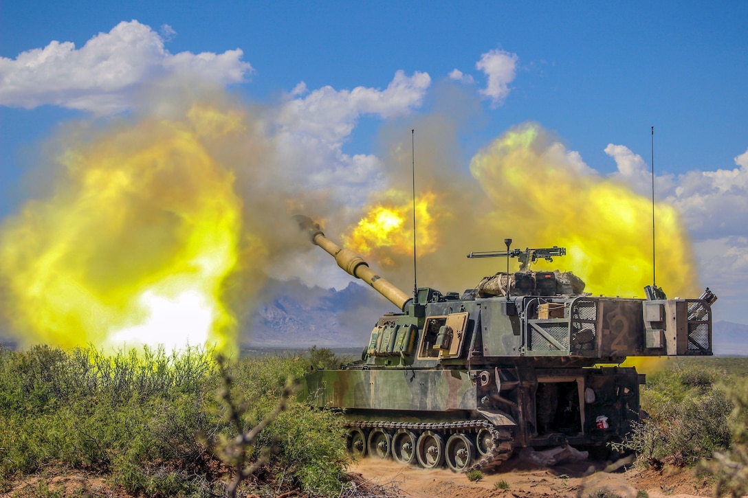 Flames shoot out from a tank's gun as it fires in a field.