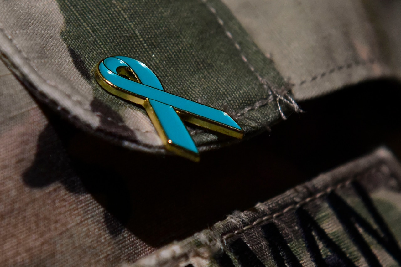 A teal ribbon pin adorns a pocket flap on a soldier's uniform.