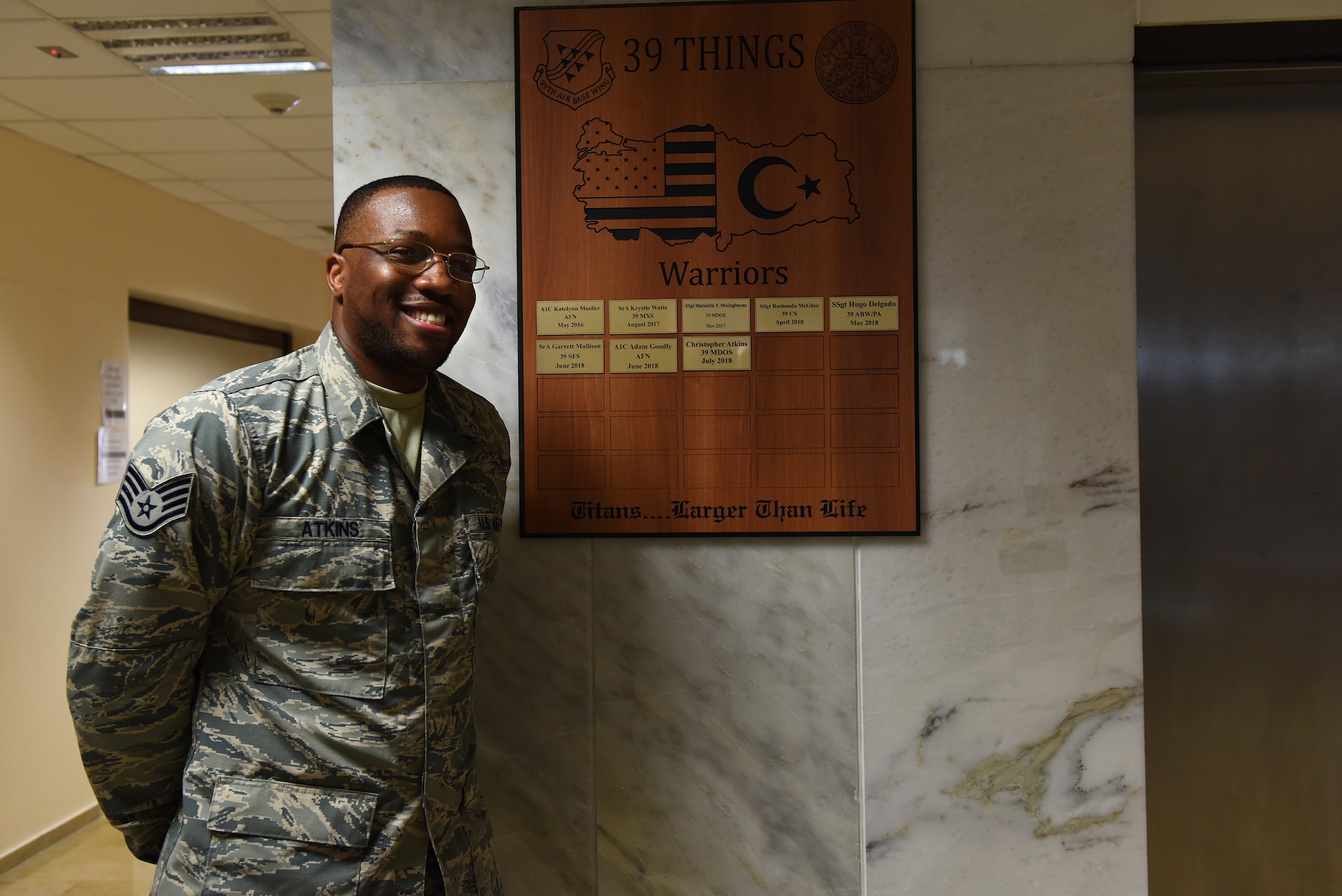 U.S. Air Force Staff Sgt. Christopher Atkins stands next to a inscribed plaque on the medical "Hall of Fame" after completing the Titan University Warrior Program at Incirlik Air Base, Turkey, July 31, 2018.