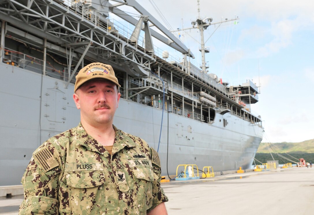 Navy Petty Officer 2nd Class Andrew Pluss, an electrician’s mate assigned to the Guam-based submarine tender USS Frank Cable, stands in front of the ship at Naval Base Guam, July 18, 2018. Pluss helped the victim of an auto-pedestrian crash in Guam July 16. Navy photo by Alana Chargualaf