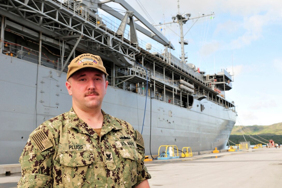 A sailor poses for a picture in front of a ship.