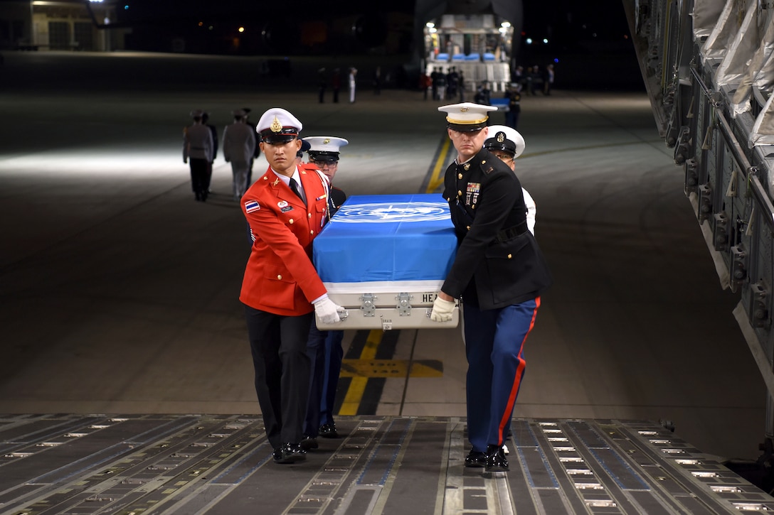 U.S. and foreign service members carry a box with a U.N. flag over it.