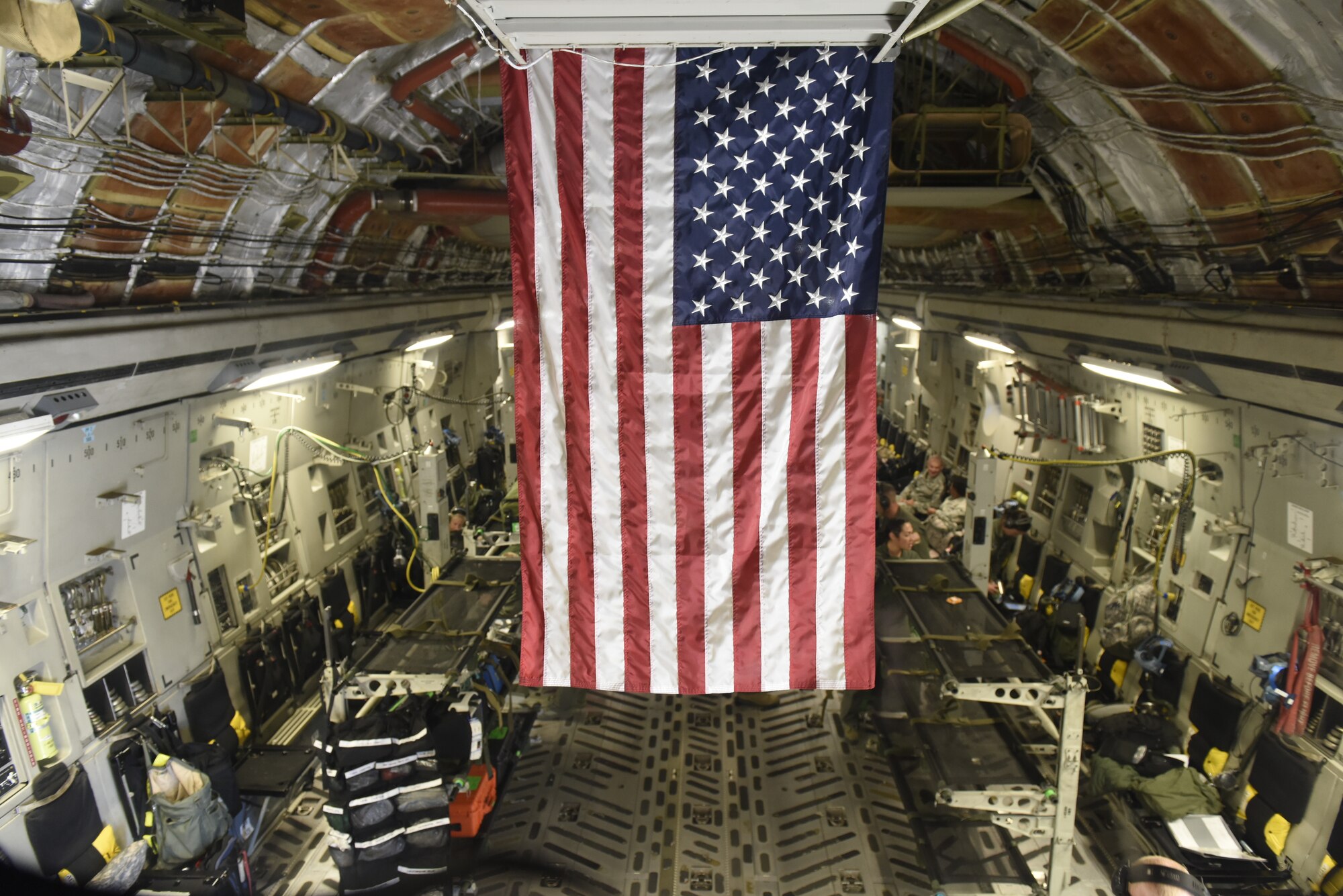 The American flag hangs from the roof a North Carolina Air National Guard C-17 Globemaster III, while members of the 156th Aeromedical Evacuation Squadron prepare for takeoff in the background at North Carolina Air National Guard Base, Charlotte Douglas International Airport, for a flight to Volk Field Air National Guard Base, Wisconsin, for a training exercise, July 9, 2018. (U.S. Air Force photo by Tech. Sgt. Nathan Clark)