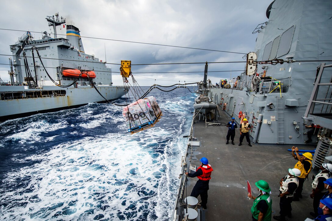 Sailors guide pallets of food and supplies during a replenishment-at-sea.