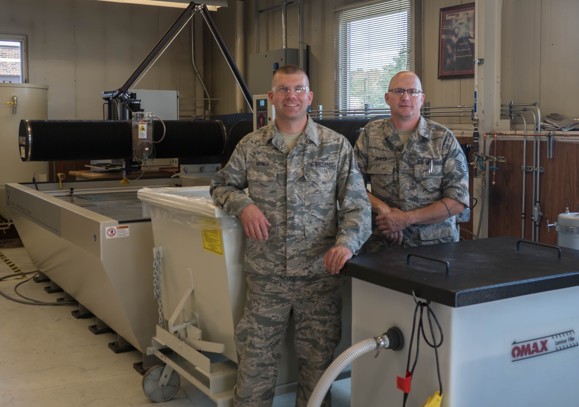Tech. Sgt. Tyler Horner (left) and Master Sgt. Eric Johnson stand by the new Water Jet Machining Center at the 934th Maintenance Squadron Metal Fabrication shop. (Air Force Photo/Paul Zadach)