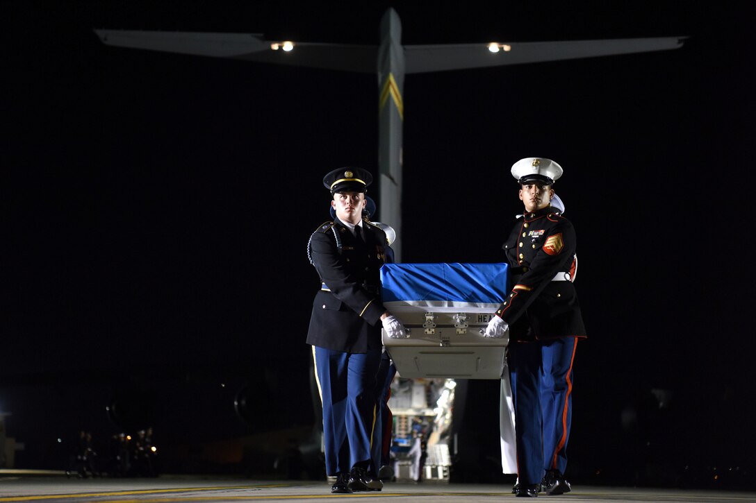 Service members carry a box with a U.N. flag away from an aircraft.