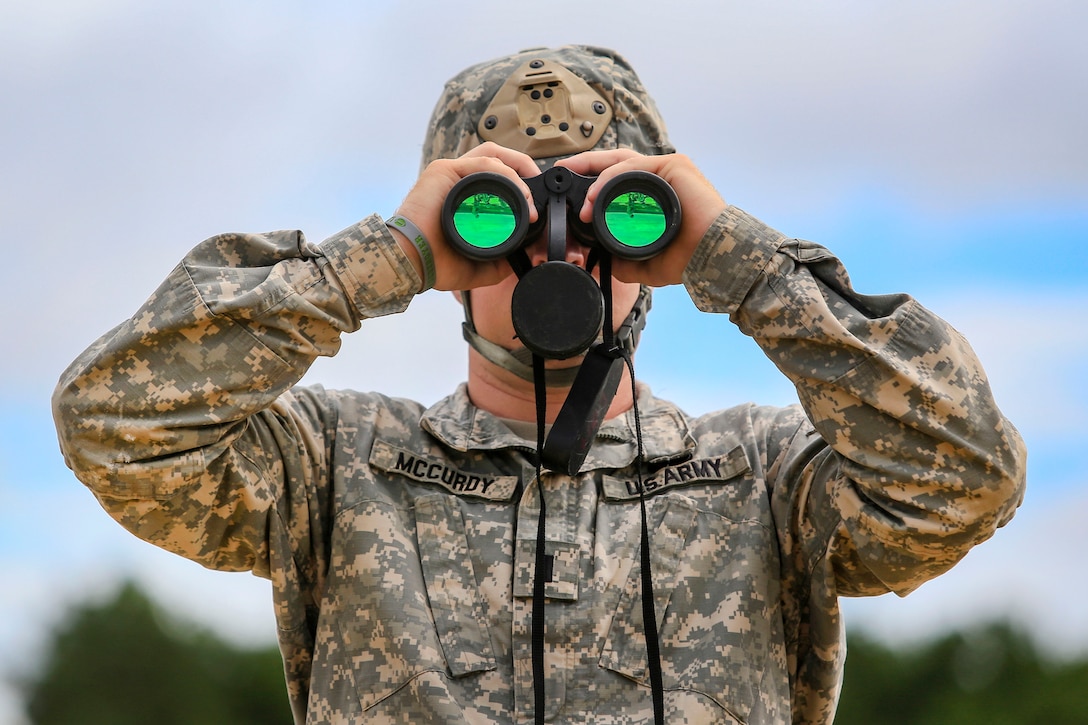 A soldier uses binoculars to observe targets down range.