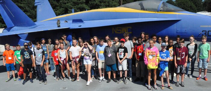 IMAGE: KING GEORGE. Va. (June 29, 2018) - Middle school students stand in front of an F-18 used as a ground plane for testing and evaluating the hazards of electromagnetic radiation to ordnance at the Naval Surface Warfare Center Dahlgren Division (NSWCDD) Electromagnetic Environmental Effects test site. The students toured NSWCDD in conjunction with their academy activities at the 2018 STEM Summer Academy. They saw the real-world applications during their tour that also featured the electromagnetic railgun, laser lethality laboratory, Potomac River Test Range, and vehicle integration technologies.