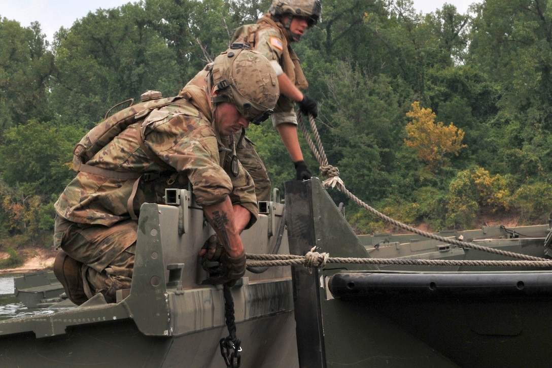 Soldiers use towing ropes to secure a portion of a temporary floating bridge.