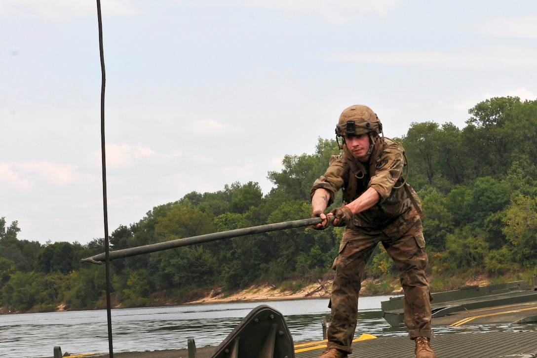 A soldier uses a grappling pole hook to retrieve a securing rope.