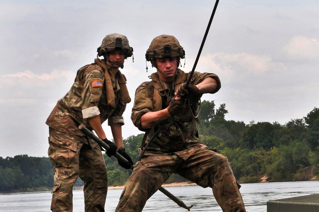 A soldier pulls on a cable while shifting a ramp to assemble a temporary floating bridge.