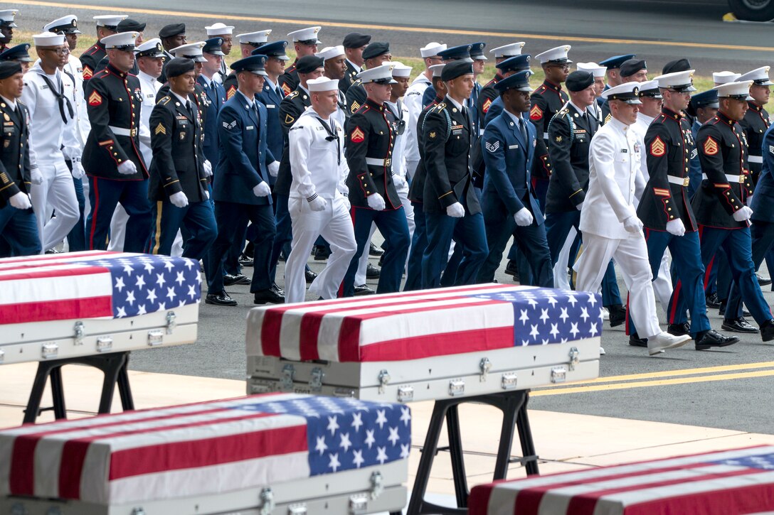 Service members walk in formation past caskets.