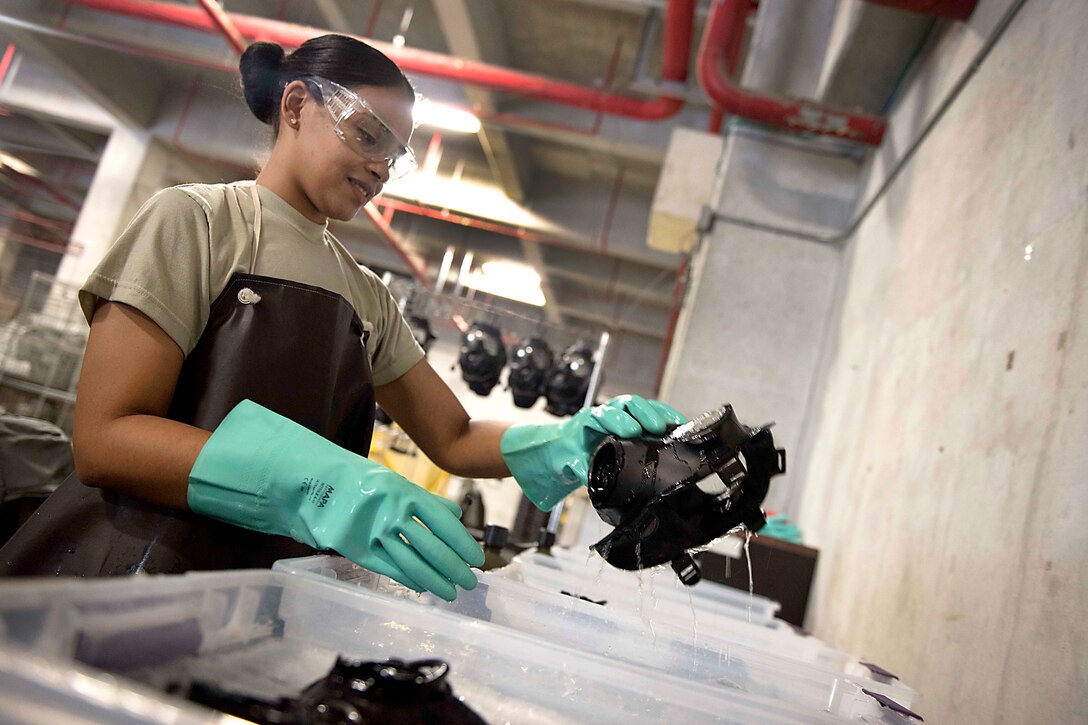 An airman pulls a gas mask out of a container of water.