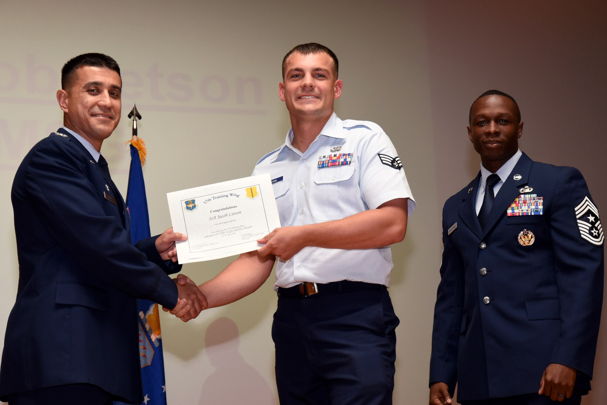 U.S. Air Force Co. Ricky Mills, 17th Training Wing commander, presents the Airman of the Quarter certificate to Senior Airman Jacob Letson, with Chief Master Sgt. Lavor Kirkpatrick, 17th TRW command chief, during the 17th TRW quarterly awards ceremony at the Base Theater on Goodfellow Air Force Base, Texas July 31, 2018. (U.S. Air Force photo by Airman 1st Class Seraiah Hines/Released)