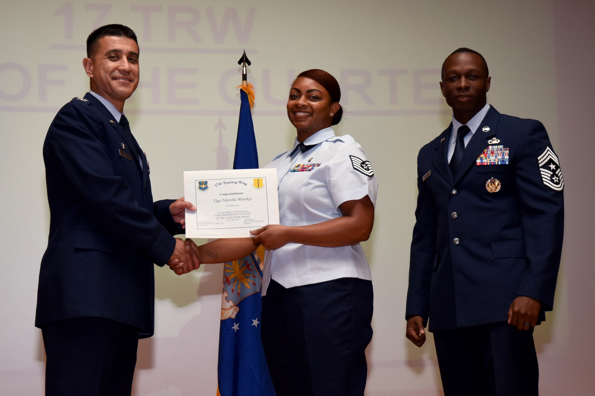 U.S. Air Force Col. Ricky Mills, 17th Training Wing commander, presents the Noncommissioned Officer of the Quarter certificate to Tech Sgt. Natosha Mansker with Chief Master Sgt. Lavor Kirkpatrick, 17th TRW command chief, during the 17th TRW quarterly awards ceremony at the Base Theater on Goodfellow Air Force Base, Texas, July 31, 2018. (U.S. Air Force photo by Airman 1st Class Seraiah Hines/Released)