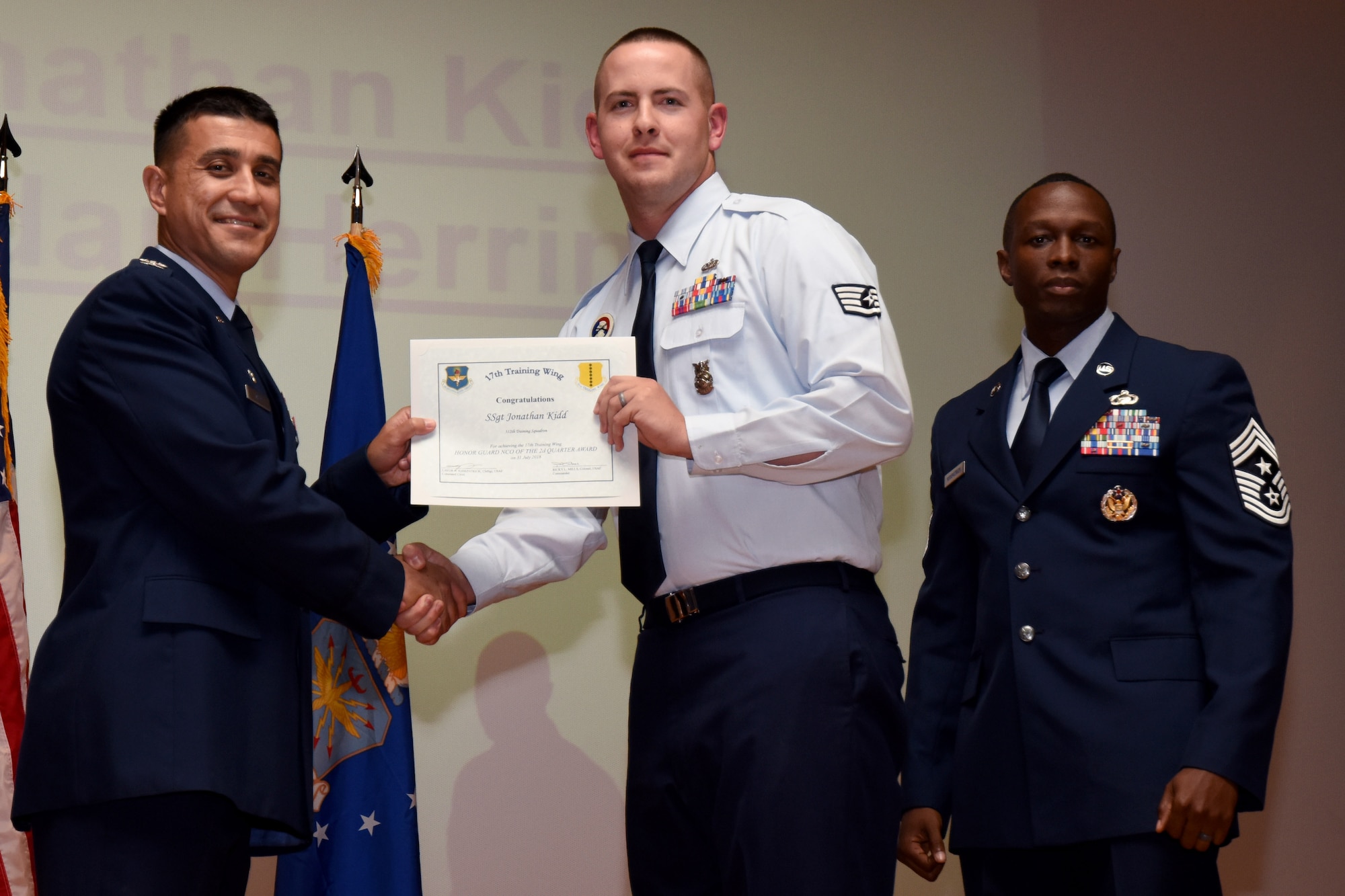 U.S. Air Force Col. Ricky Mills, 17th Training Wing commander, presents the Honor Guard Noncommissioned Officer of the Quarter certificate to Jonathan Kidd, with Chief Master Sgt. Lavor Kirkpatrick, 17th TRW command chief, during the 17th TRW quarterly awards ceremony at the Base Theater on Goodfellow Air Force Base, Texas, July 31, 2018. (U.S. Air Force photo by Airman 1st Class Seraiah Hines/Released)