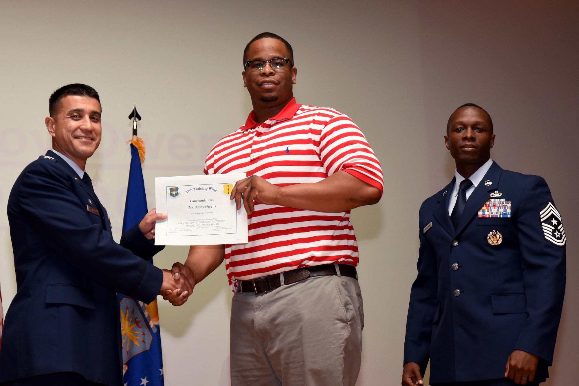 U.S. Air Force Col. Ricky Mills, 17th Training Wing commander, presents the Civilian Non-supervisory Category I of the Quarter certificate to Jacoy Owens, with Chief Master Sgt. Lavor Kirkpatrick, 17th TRW command chief, during the 17th TRW quarterly awards ceremony at the Base Theater on Goodfellow Air Force Base, Texas, July 31, 2018. (U.S. Air Force photo by Airman 1st Class Seraiah Hines/Released)
