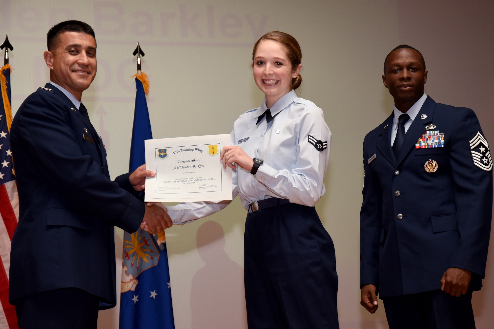 U.S. Air Force Col. Ricky Mills, 17th Training Wing commander, presents the Dormitory Room of the Quarter certificate to Airman 1st Class Haden Barkley, with Chief Master Sgt. Lavor Kirkpatrick, 17th TRW command chief, during the 17th TRW quarterly awards ceremony at the Base Theater on Goodfellow Air Force Base, Texas, July 31, 2018. (U.S. Air Force photo by Airman 1st Class Seraiah Hines/Released)