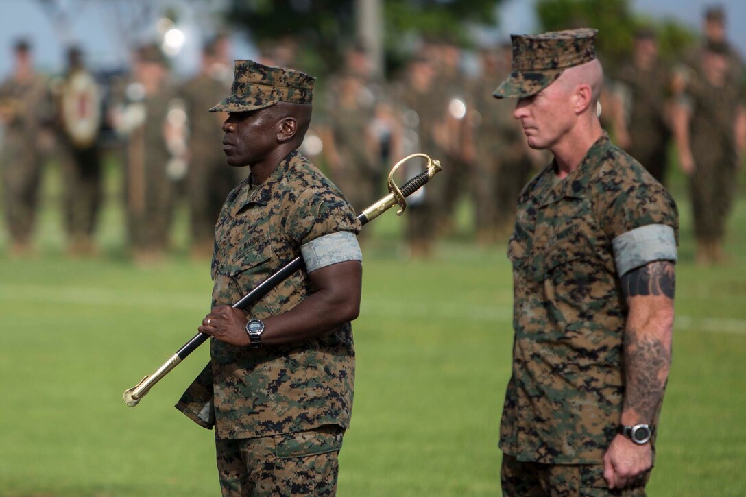 Sgt. Maj. James E. Monroe, left, stands with the noncommissioned officer sword of office before ceremoniously passing it to Sgt. Maj. Jason Hammock, right, during a relief and appointment ceremony for Headquarters Regiment, 3rd Marine Logistics Group, Aug. 3, 2018 at Camp Kinser, Okinawa, Japan. Sgt. Maj. James E. Monroe ceremoniously transferred accountability and authority of enlisted Marines to Hammock during the ceremony.. Hammock is a native of Miami, Florida. (U.S. Marine Corps photo by Lance Cpl. Jamin M. Powell)