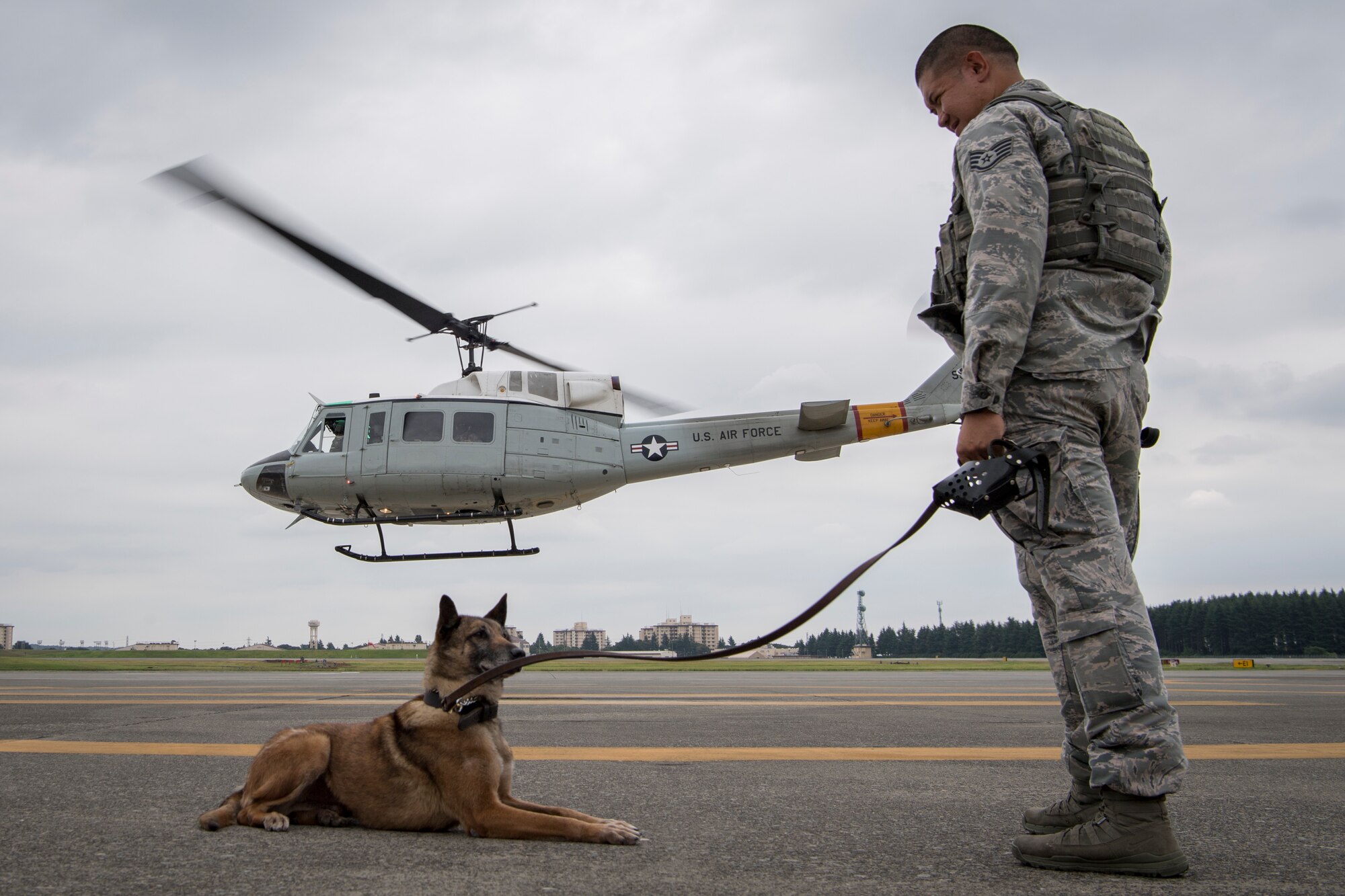 Staff Sgt. Michael Dacoron, 374th Security Forces Squadron military working dog handler, watches with Diesel, 374 SFS MWD, as a UH-1N helicopter takes off during a 459th Airlift Squadron MWD familiarization flight July 26, 2018, at Yokota Air Base, Japan.