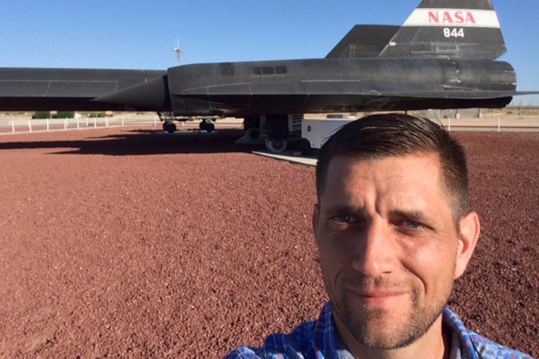 A man takes a selfie with a NASA aircraft in the background.