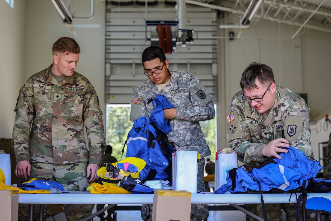 Three National Guardsmen check their equipment on a table.