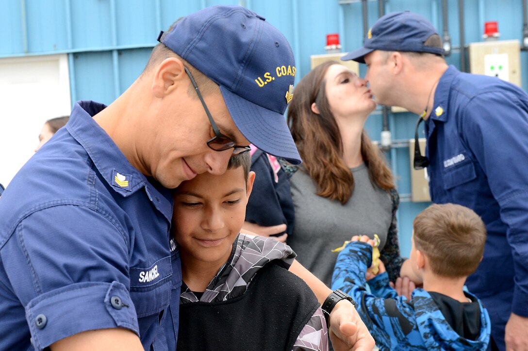 A man hugs his son, as a couple kisses in the background.