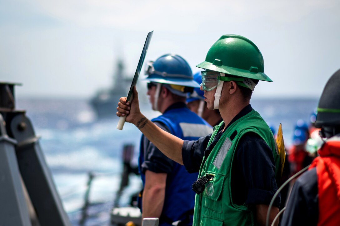 A sailor signals to the Canadian supply ship MV Asterix from the guided-missile destroyer USS Dewey.
