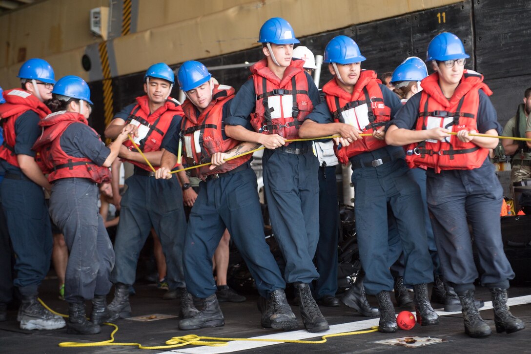 Sailors pull on a heaving line during the recovery of a combat rubber raiding craft.