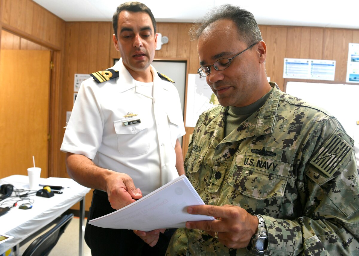 Military leaders converse while looking at a computer screen.